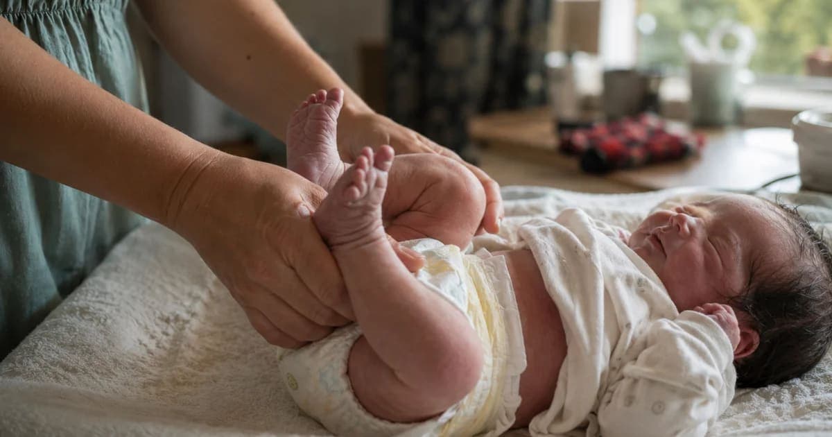 A parent's hands gently changing a newborn baby's diaper on a soft linen mat in a sunlit nursery, showing the routine care and frequency of newborn diapering.
